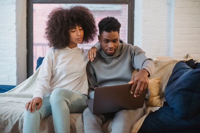 Black couple sitting on sofa and looking at laptop