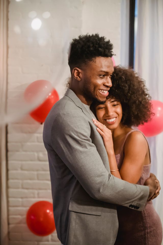 Smiling black couple dancing while embracing in loft with balloons